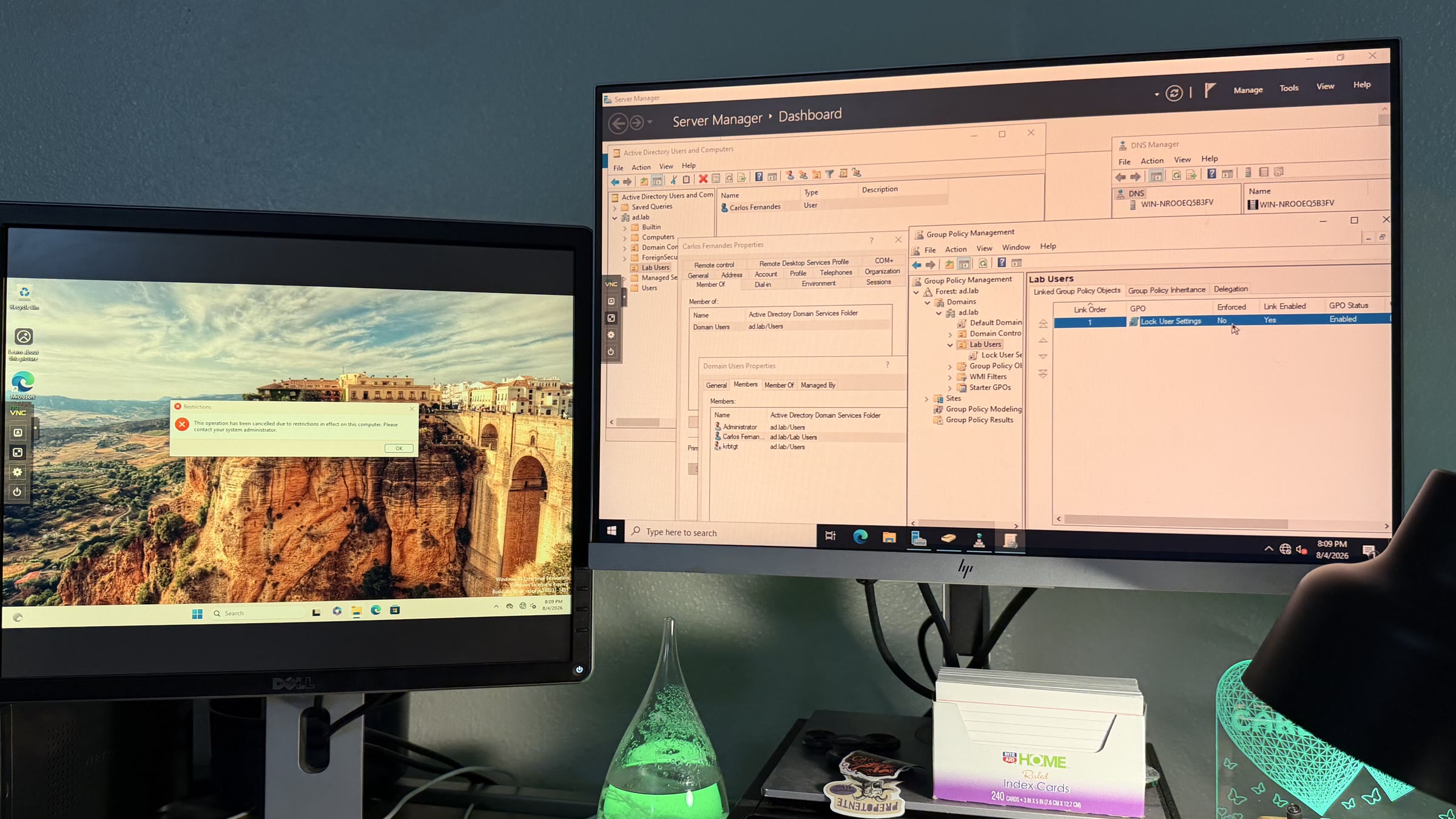 Active Directory homelab with the domain controller tools on one screen and the client machine showing a GPO-based Control Panel restriction on the other